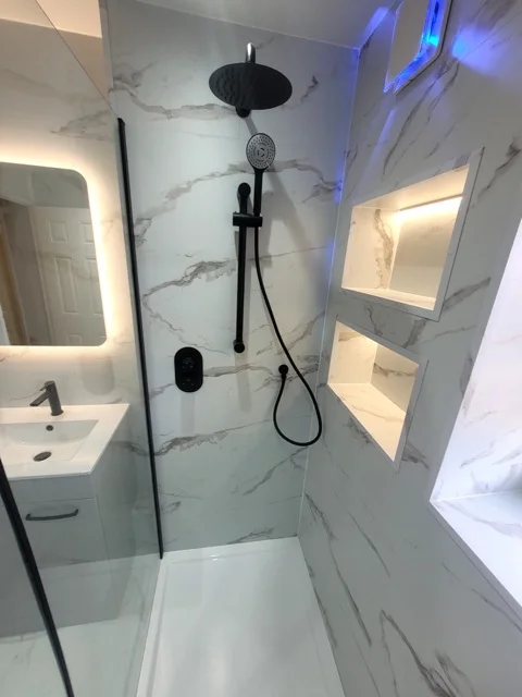 Black shower fittings and backlit mirror beside SPC marble walls in Ramsbottom