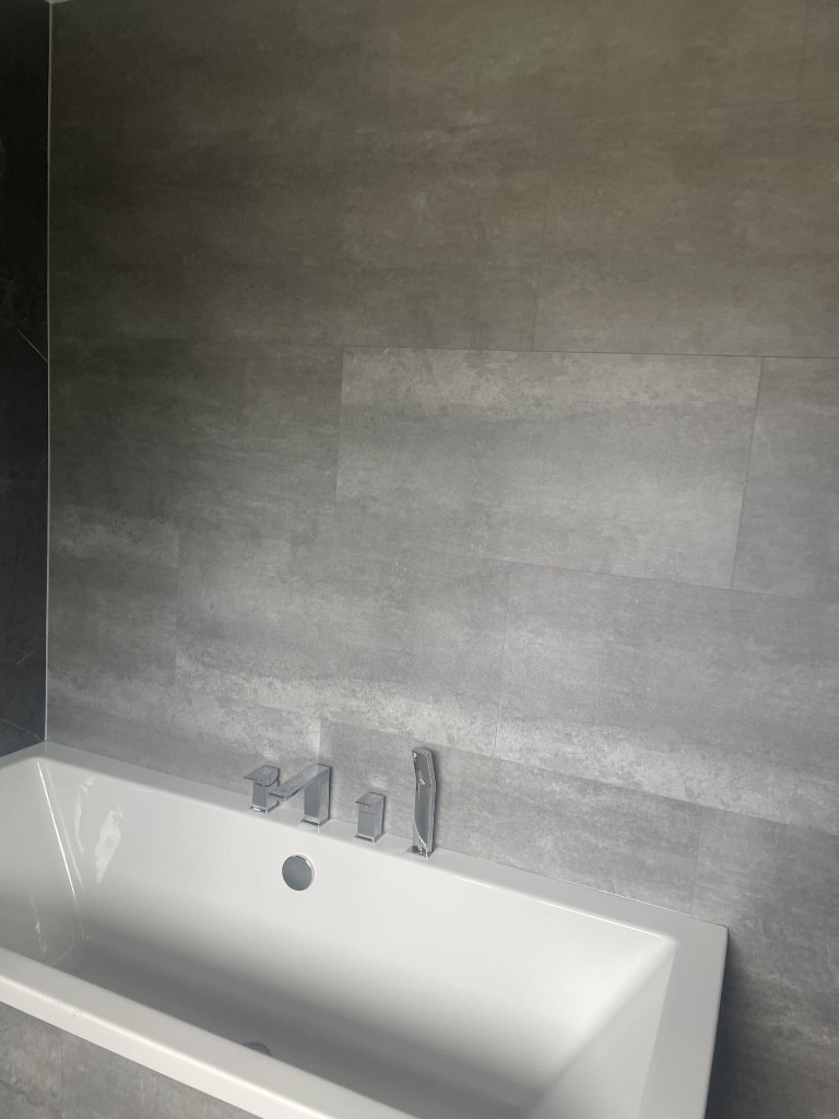 Built-in bath with chrome deck taps and grey stone wall tiles in Sacriston