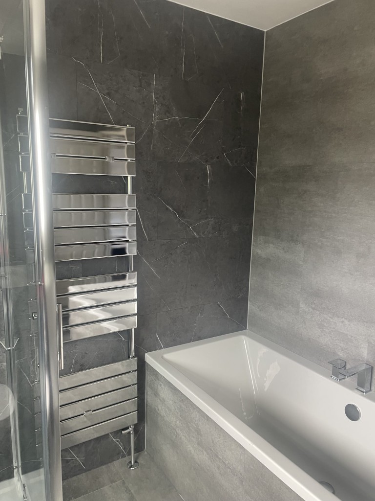 Built-in bath and chrome towel rail with marble and stone tiles in Sacriston