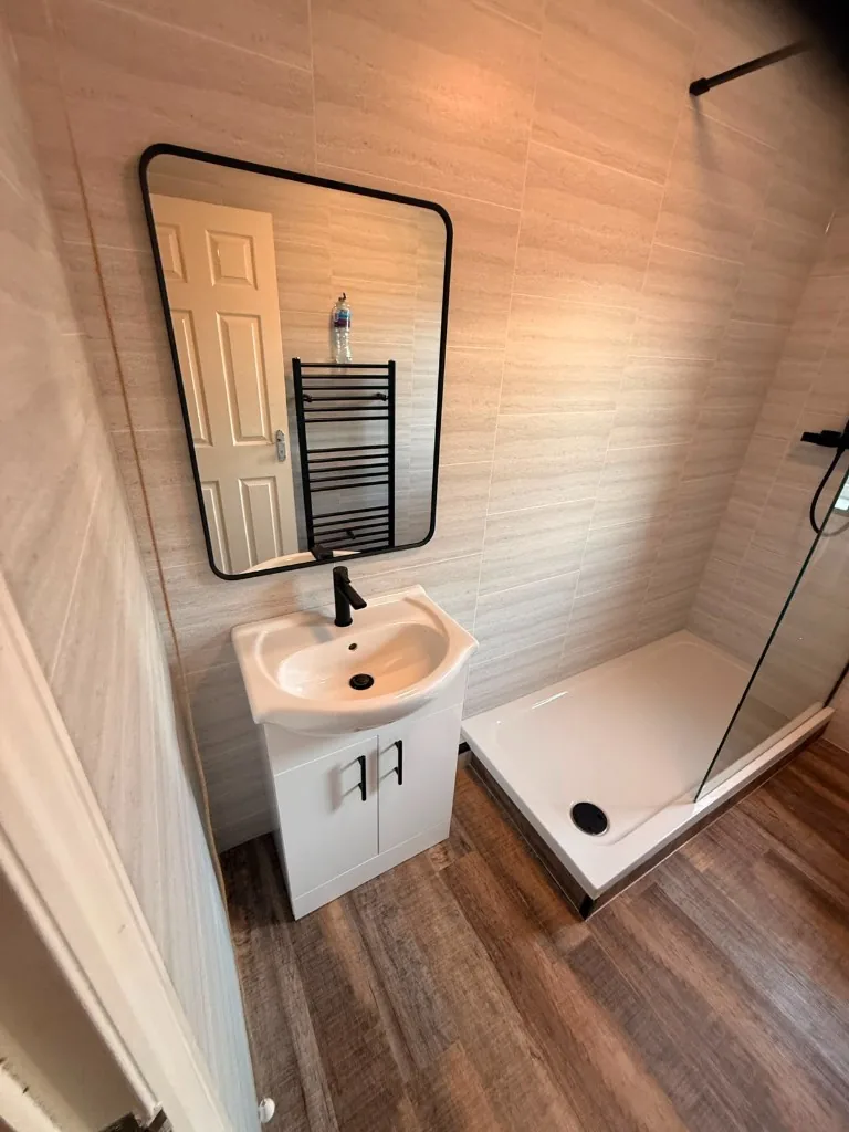 Walk-in shower with black fittings beside vanity and wood-effect flooring in Tow Law