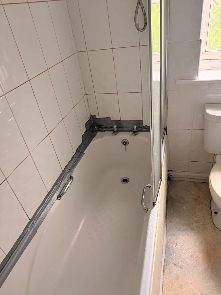 Old bathtub with duct-taped seal and dated tiles before renovation in Tow Law