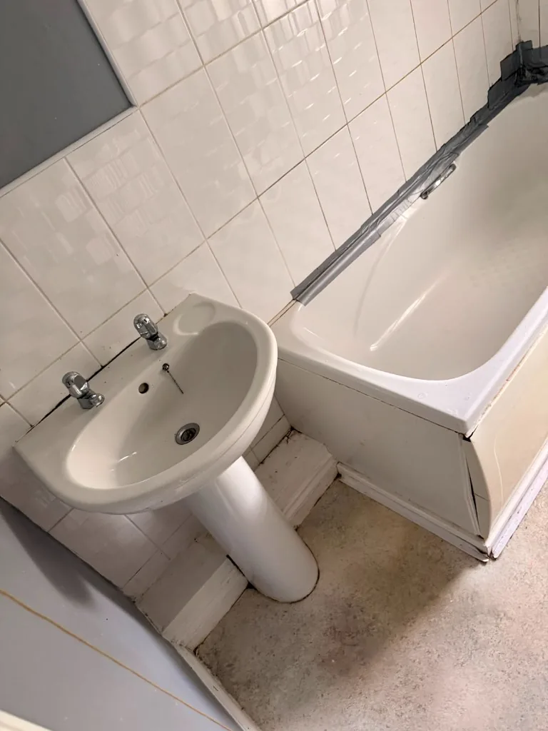 Old pedestal sink and bathtub with temporary duct-tape seal in Tow Law bathroom