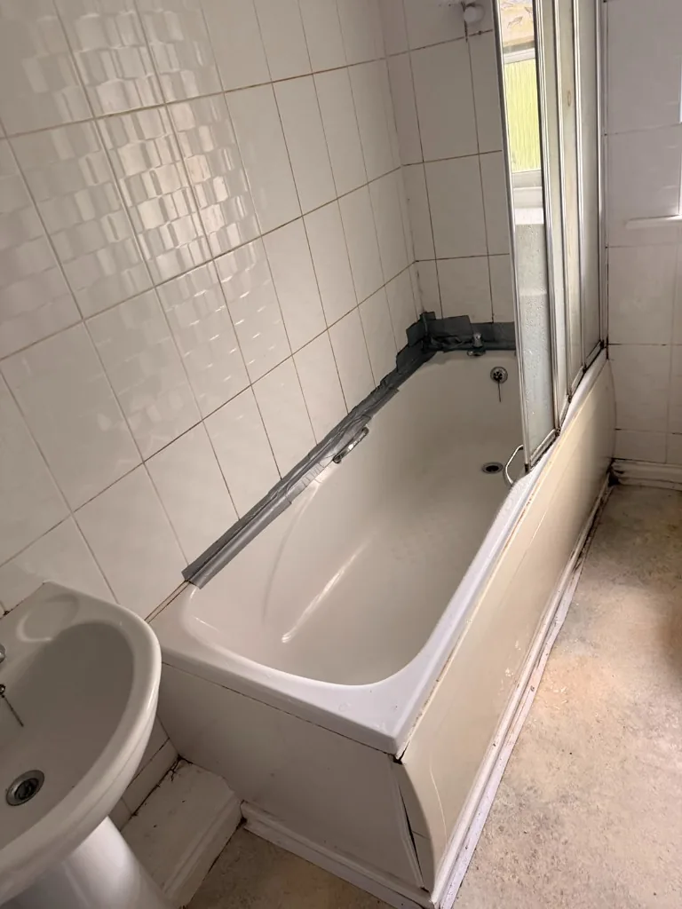 Cracked bath panel and duct-taped wall joint before bathroom refit in Tow Law