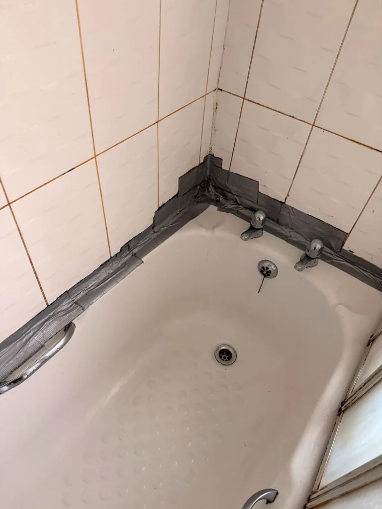 Mouldy tiles and duct tape sealing a leaking bath edge before renovation in Tow Law