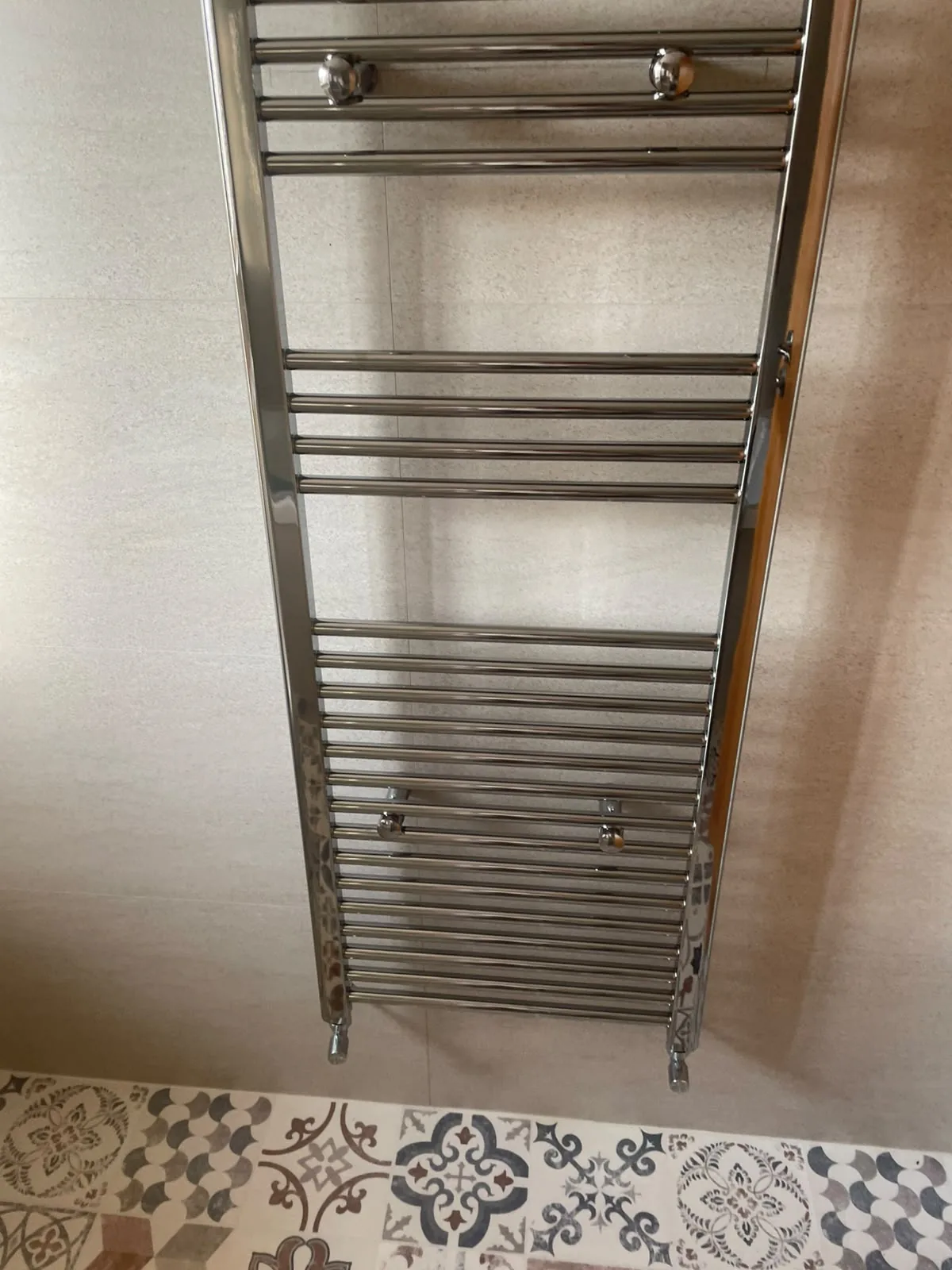 Chrome heated towel rail against SPC tiles and patterned vinyl flooring in Wingate