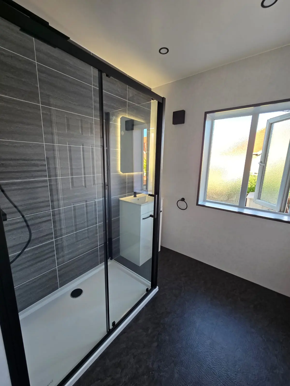 Finished Sunderland bathroom with black shower cubicle, dark grey tile-effect feature wall and backlit LED mirror