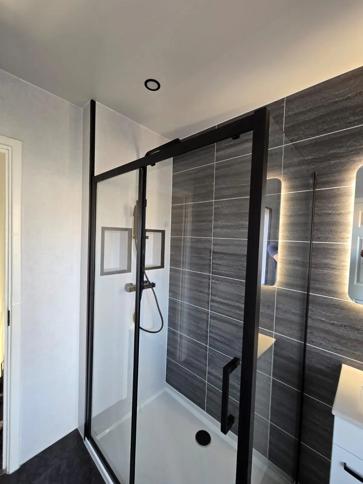 Black-framed shower cubicle with rainfall shower against dark grey tile-effect cladding in Sunderland