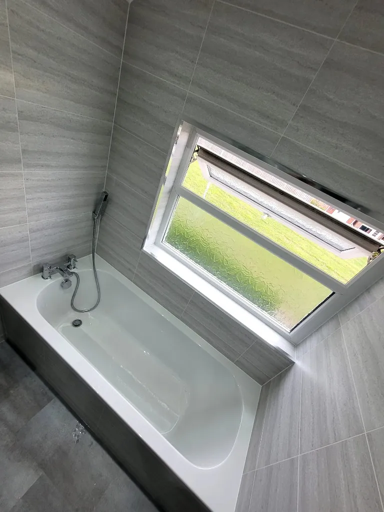 Built-in bath with grey cladding and frosted window in Durham bathroom