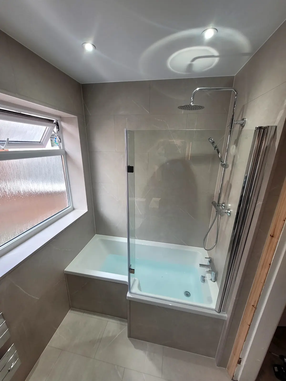 L-shaped shower bath with glass screen and chrome rainfall shower in Sunderland