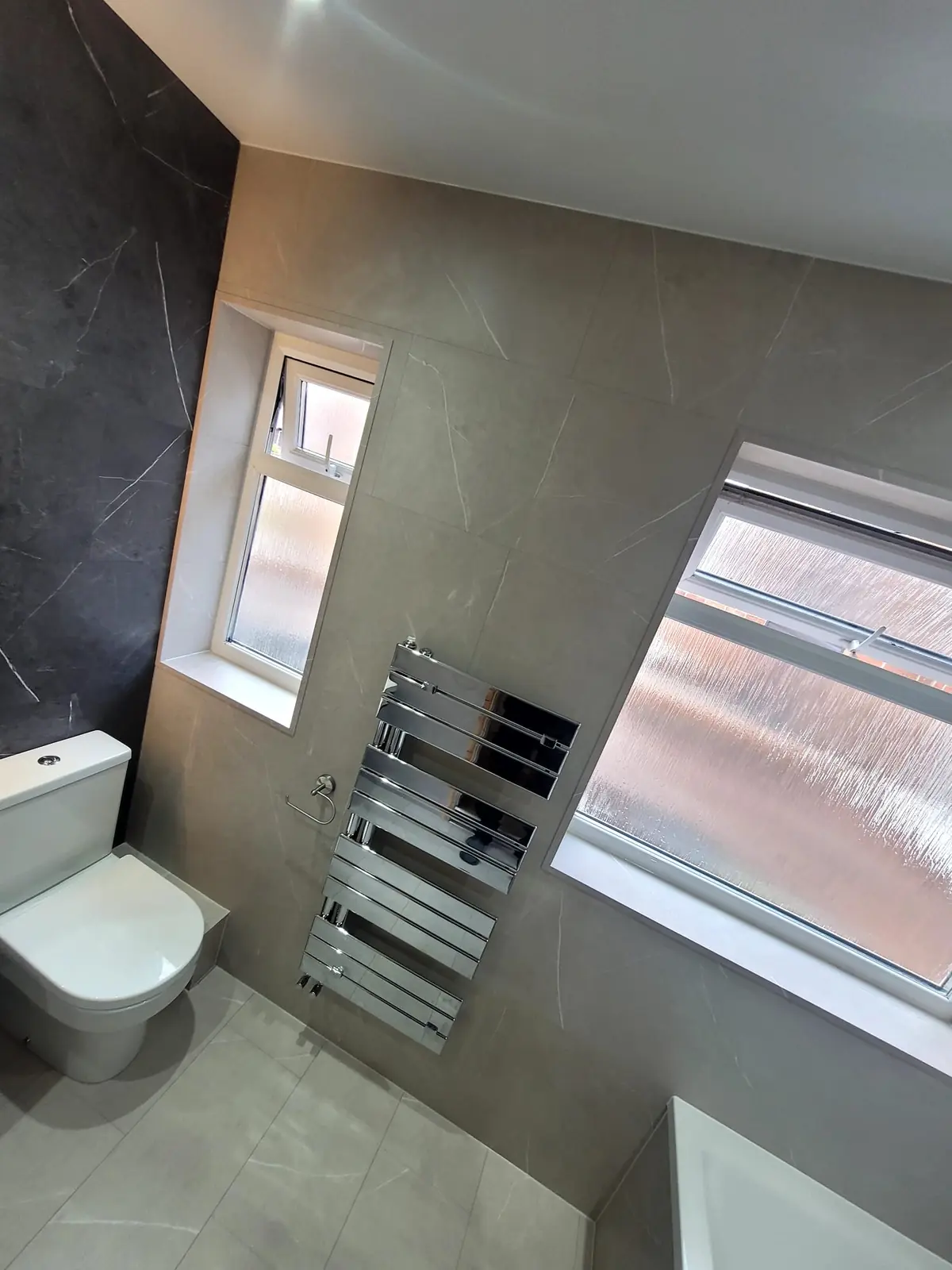 Polished chrome designer heated towel radiator between frosted windows in Sunderland