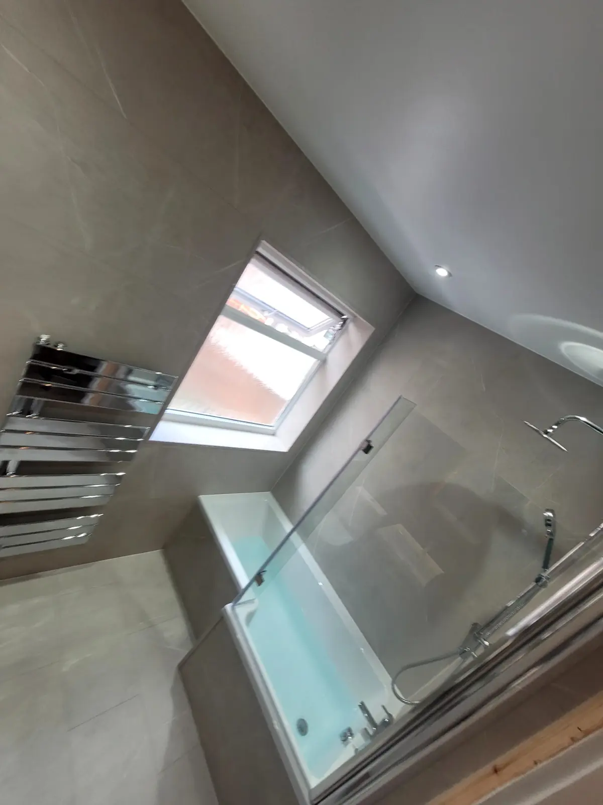L-shaped bath with glass shower screen beside chrome designer radiator in Sunderland