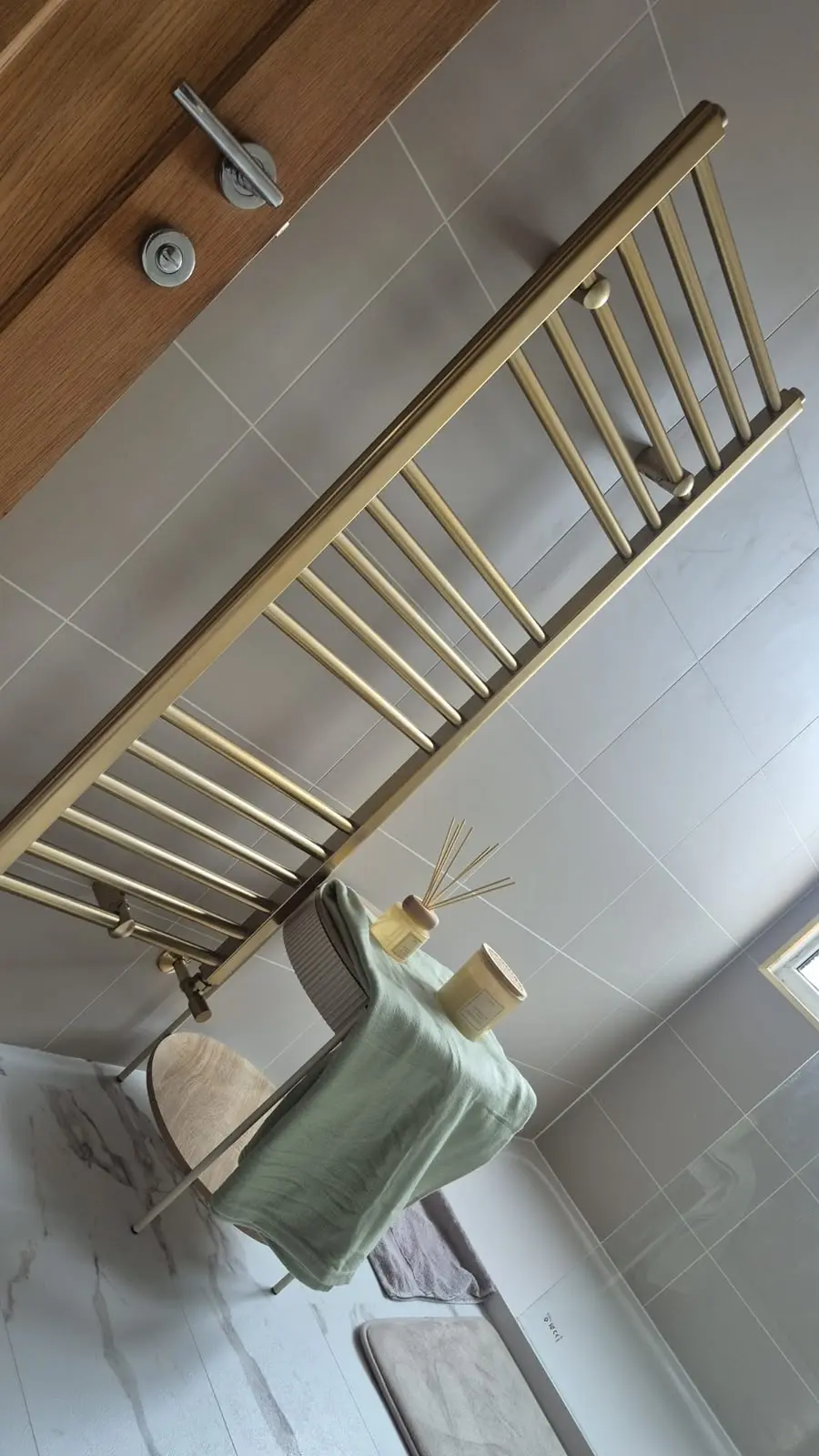Brushed brass heated towel rail with stool, sage towel and accessories on Calacatta SPC flooring