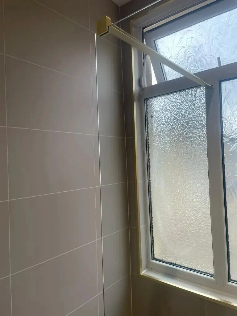 Frosted privacy window with brushed brass shower-screen support against taupe cladding in Darlington