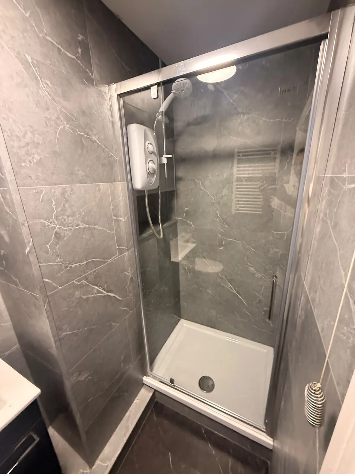 Glass shower cubicle with recessed niche and electric shower against SPC marble wall panels in Durham