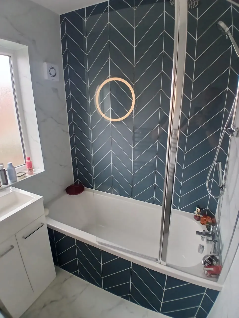 Finished Jarrow bathroom with green herringbone bath feature, circular LED mirror, white marble cladding and two-part shower screen