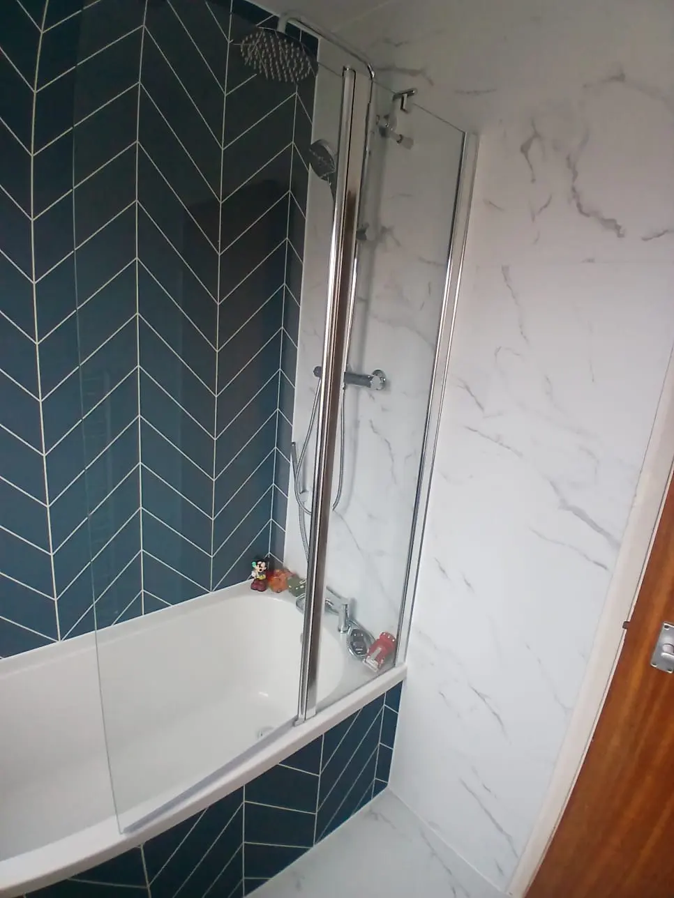 Bath with green herringbone side panel and wall, chrome rainfall shower and two-part glass screen in Jarrow