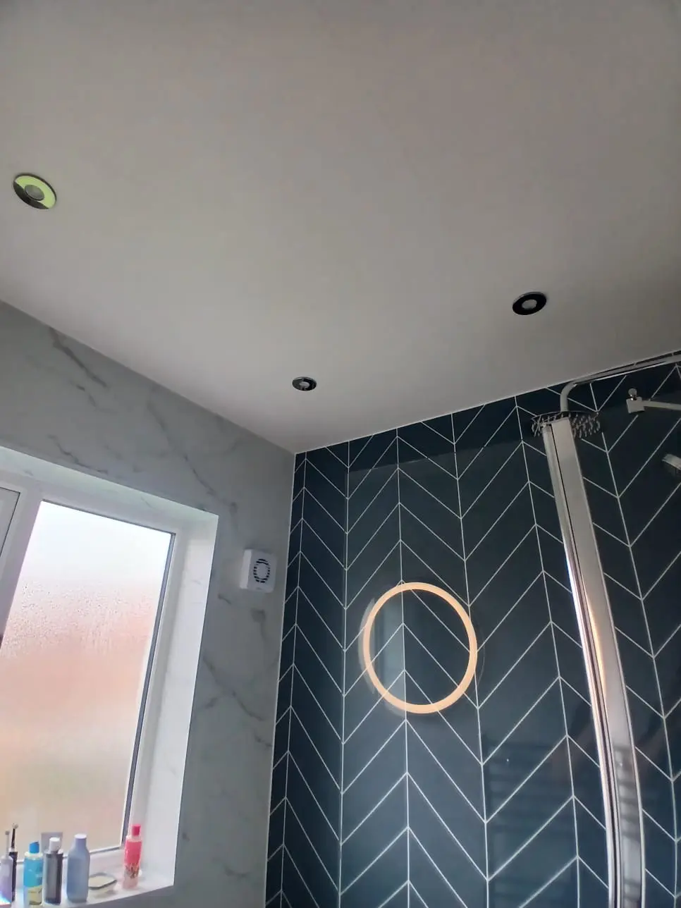 Circular LED mirror mounted on green herringbone feature wall above the bath in Jarrow