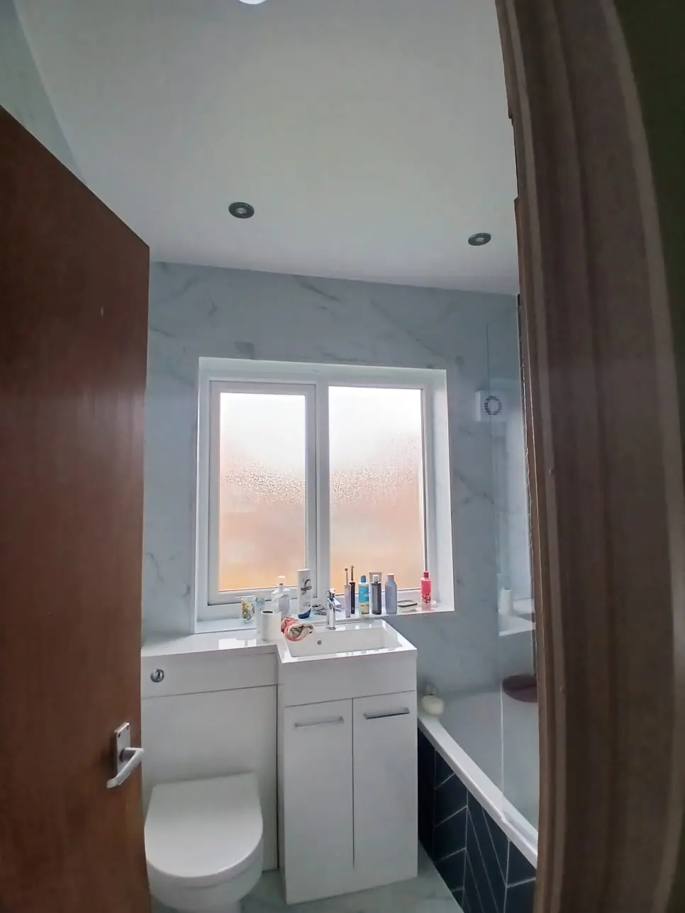 Jarrow bathroom from the doorway — white marble cladding, vanity under the window and green herringbone bath panel