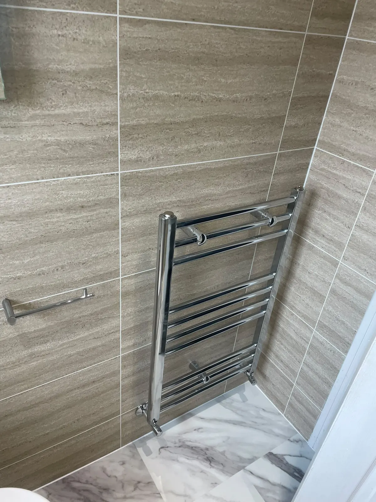 Chrome heated towel rail on Murcia cladding with white marble flooring