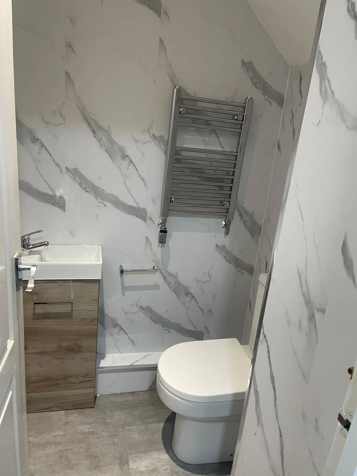 Downstairs cloakroom with oak wall-hung vanity, white marble cladding and chrome towel rail
