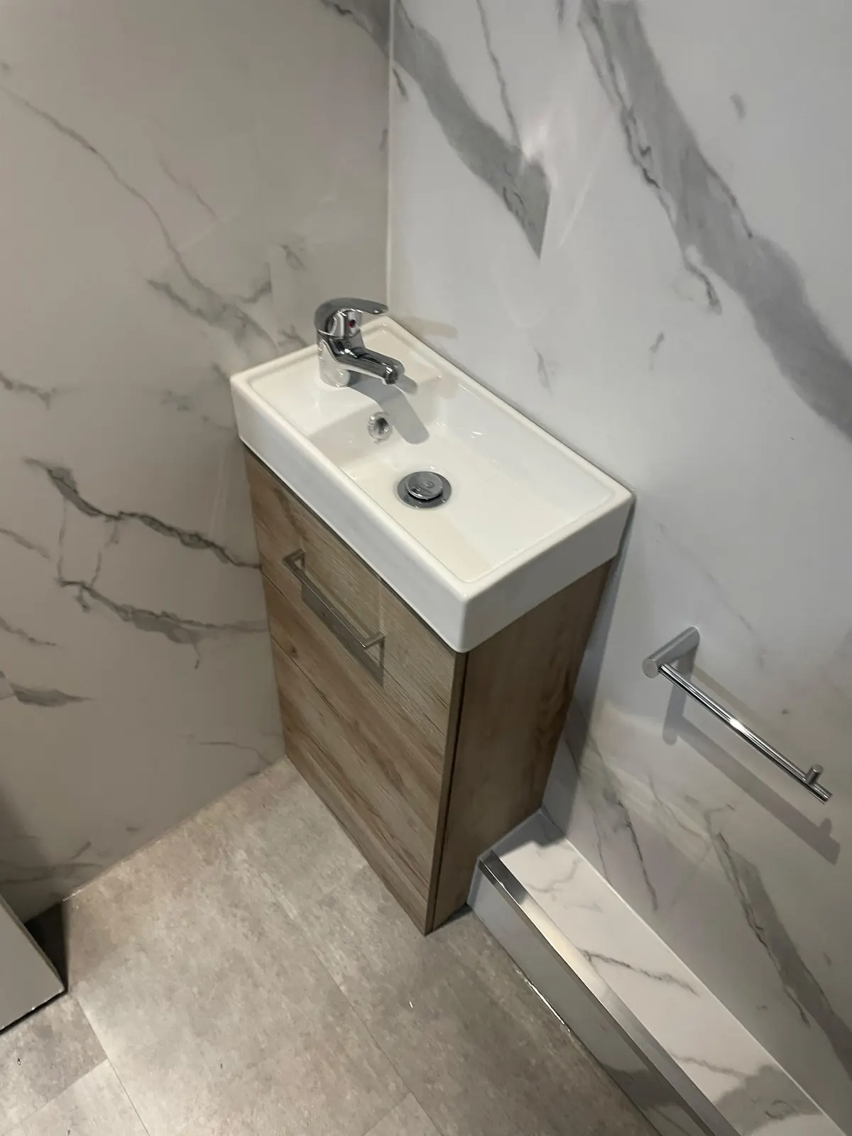 Oak wall-hung cloakroom vanity with white basin against white marble cladding