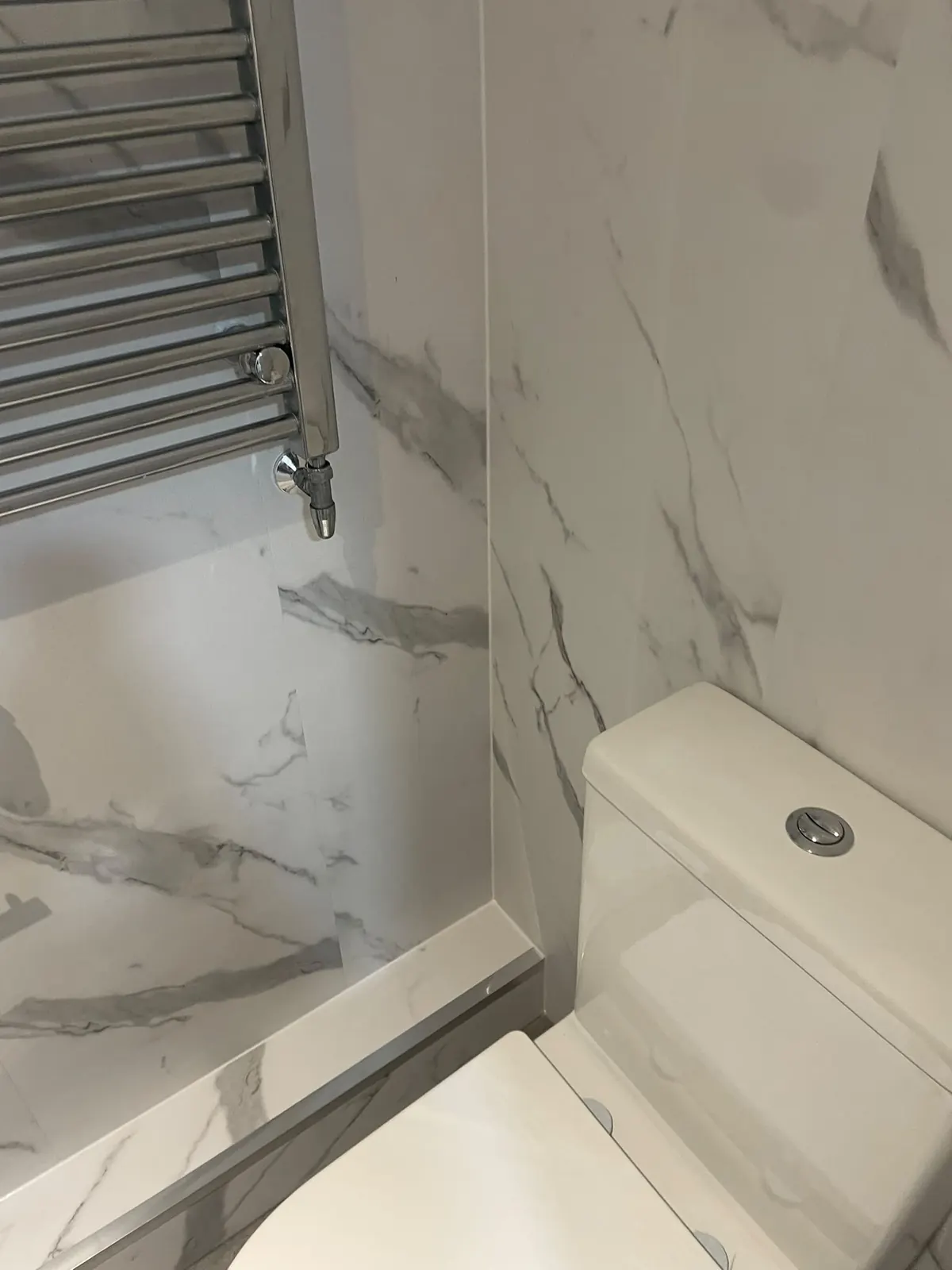 Chrome heated towel rail beside the toilet in the marble-clad downstairs cloakroom