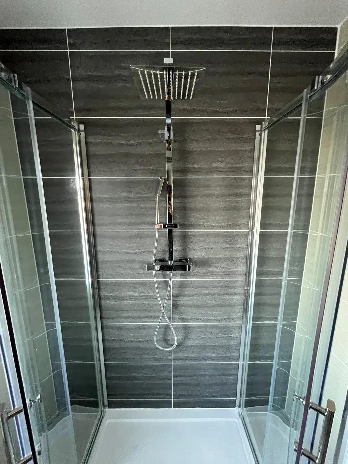 Chrome rainfall shower and handheld against dark horizontal feature tiles