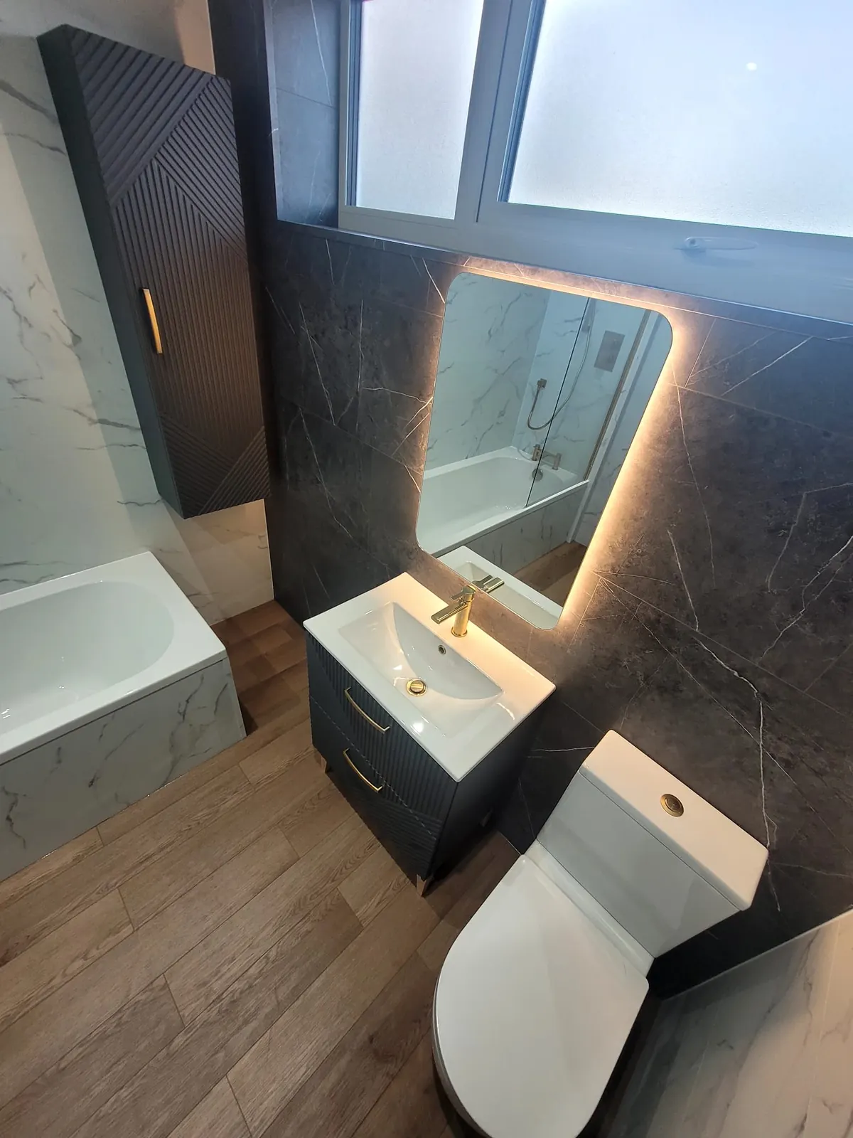 Illuminated mirror over a floating vanity with brushed brass tap in a Durham bathroom