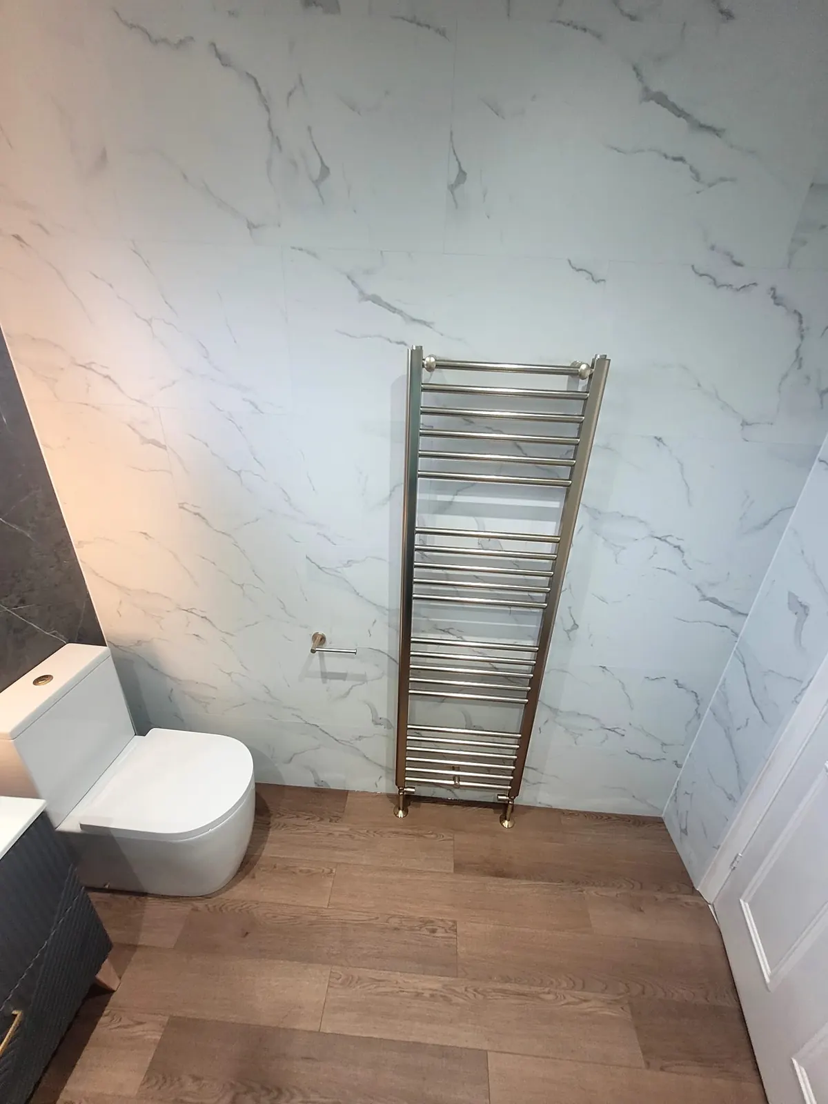 Brushed brass heated towel rail on white Trevore SPC tiles in a Durham bathroom