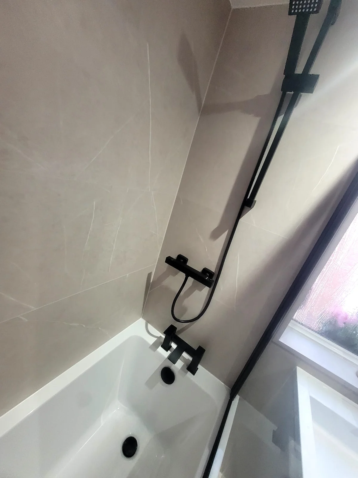Matte black rainfall shower and bath mixer against marble-effect tiles in Sunderland