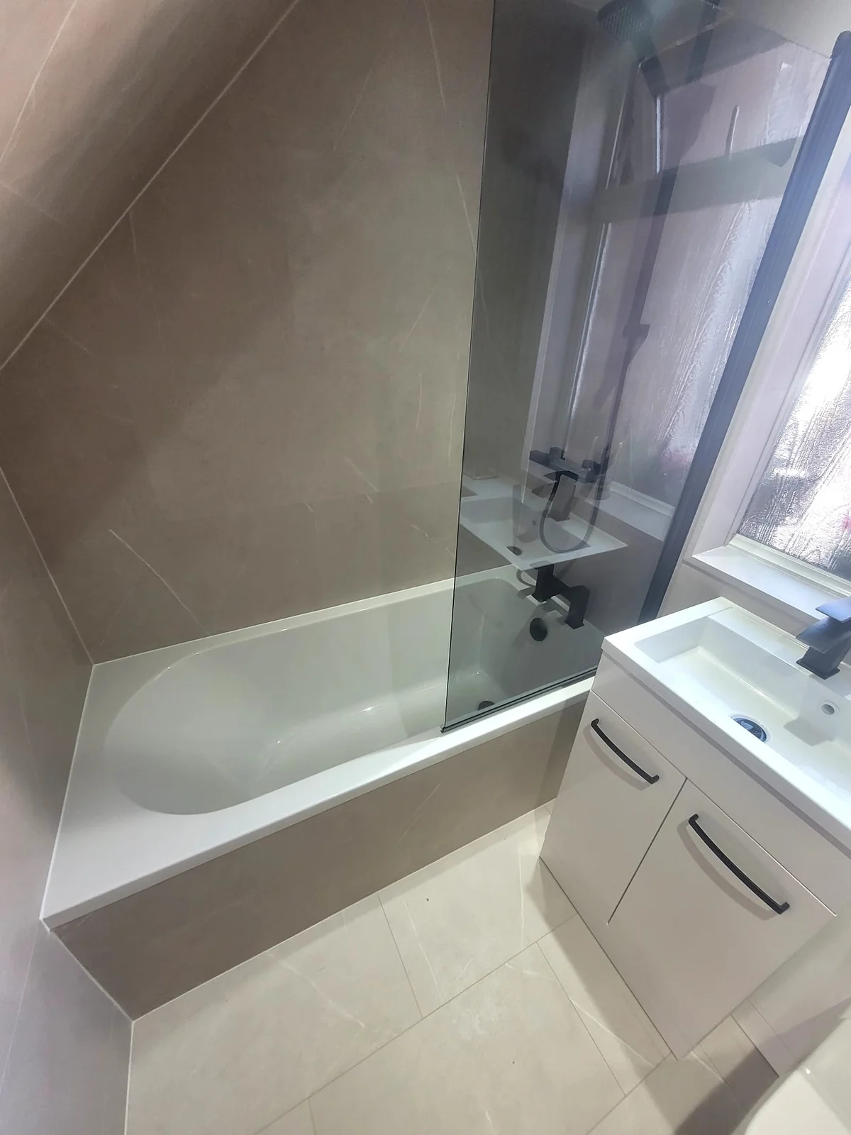 Bath with black-framed glass screen beside white vanity unit in Sunderland