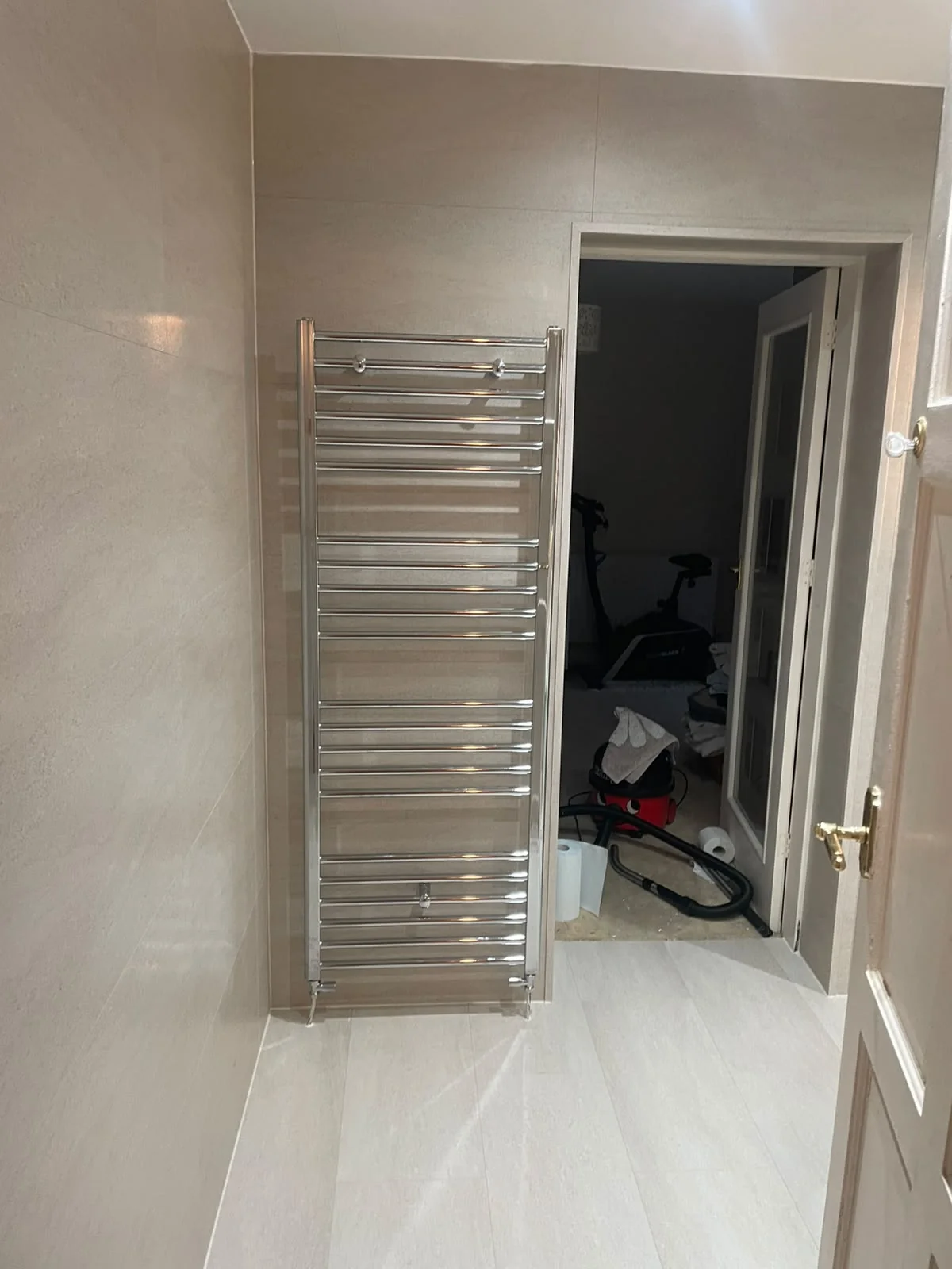 Chrome heated towel rail against beige SPC wall and floor tiles in Billingham